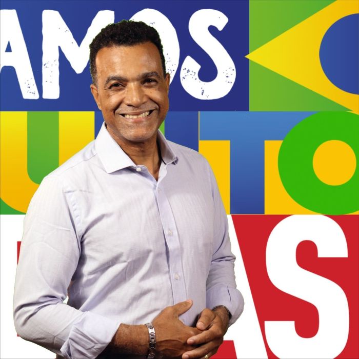 Denilson Martins é um homem preto, de cabelos pretos e barba preta. Na imagem, ele usa um colete jeans, pulseira de prata e uma camisa preta. 