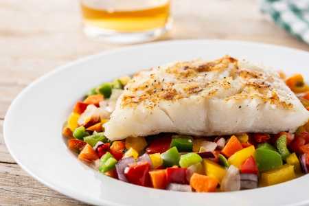 Bacalhau grelhado com legumes no prato na mesa de madeira