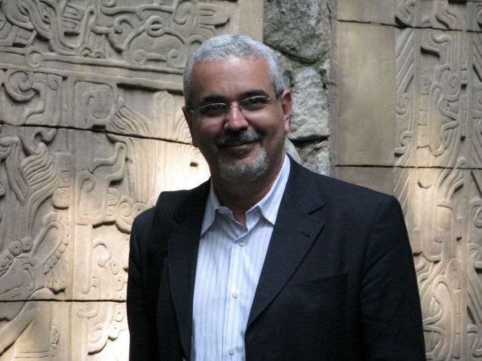 Homem branco, de cabelos brancos, barba branca, com um blazer e camisa social branca. 