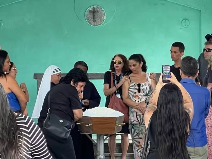 Mãe de Vaqueirinho aparece com óculos pendurado em vestido estampado, durante o sepultamento.