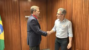 Dois homens brancos, com roupas sociais, apertam as mãos.