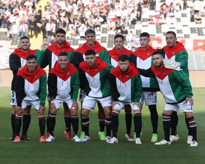 Jogadores do Palestino perfilados com agasalho em referência à bandeira da Palestina antes de jogo