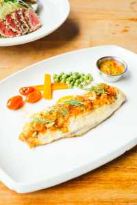 Peixe em prato branco com legumes e molho ao lado