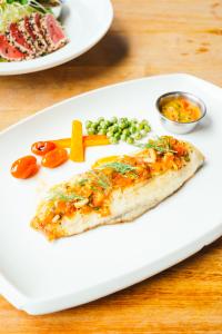 Peixe em prato branco com legumes e molho ao lado