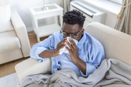 Portrait of a sick man with the flu, allergy, germs,cold coughing. Sick Man with headache sitting under the blanket with high fever and a flu, resting and drinking hot beverage