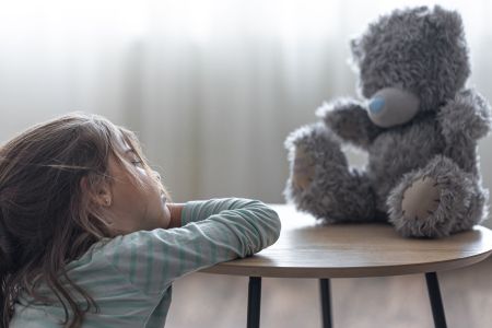 Little girl looks at her teddy bear, a child with a favorite toy on a blurred background copy space.