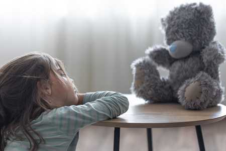 Little girl looks at her teddy bear, a child with a favorite toy on a blurred background copy space.