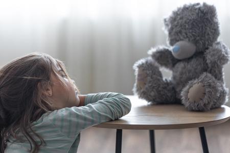 Little girl looks at her teddy bear, a child with a favorite toy on a blurred background copy space.