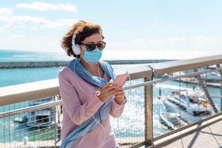 A middle-aged woman wearing a face mask standing on a bridge and listening to music