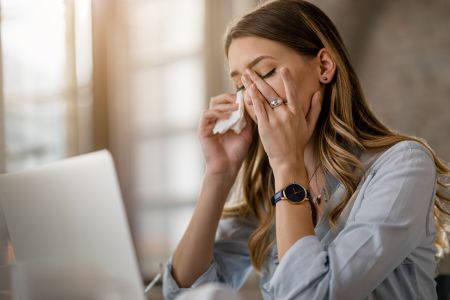 Young businesswoman with cold and flu virus having a headache while working in the office.