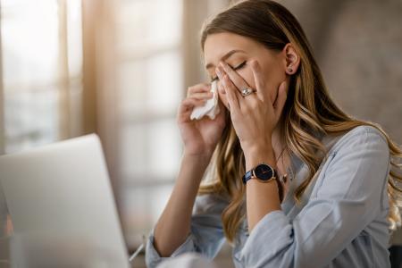 Young businesswoman with cold and flu virus having a headache while working in the office.