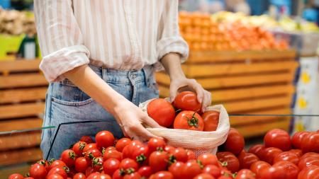 Mulher escolhendo tomates e os colocando em uma sacola reutilizável em uma feira de frutas e verduras.