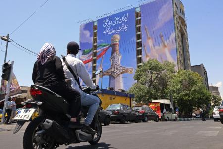 Motoristas passam por uma faixa gigante representando mísseis iranianos e uma espada pertencente ao Imã Ali, o primeiro Imã dos xiitas, na Praça Vanak, em Teerã, em 10 de junho de 2026.