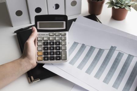 Mulher segurando calculadora e com folhas mostrando um gráfico