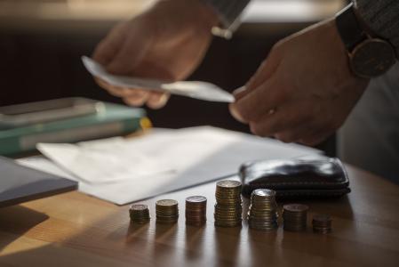 Pessoa compara juros de serviços financeiros, segura dinheiro com as duas mãos e tem uma folha de papel e moedas em cima da mesa na sua frente.