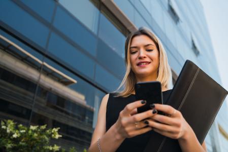 Mulher de blusa preta investindo em ações pelo celular.