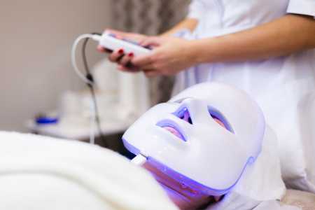The client lies in the salon on the cosmetology table with a white mask on her face