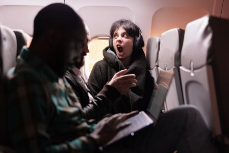 Grupo multiétnico de pessoas voando para o exterior em classe econômica, usando laptop, smartphone e fones de ouvido durante o voo ao pôr do sol. Passageiros viajando com companhia aérea comercial internacional