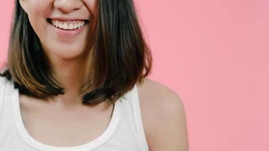 Smiling adorable Asian female with positive expression, smiles broadly, dressed in casual clothing and looking at the camera over pink background. Happy adorable glad woman rejoices success.
