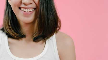 Smiling adorable Asian female with positive expression, smiles broadly, dressed in casual clothing and looking at the camera over pink background. Happy adorable glad woman rejoices success.