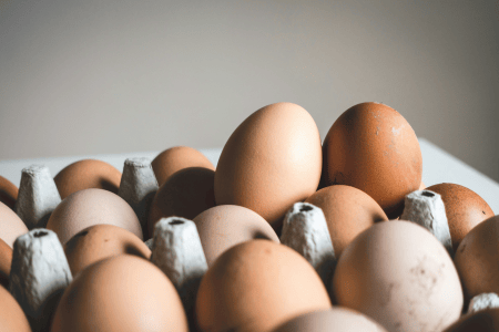 Ovos marrons e brancos dispostos em uma bandeja de papelão, com alguns ovos em destaque em primeiro plano.