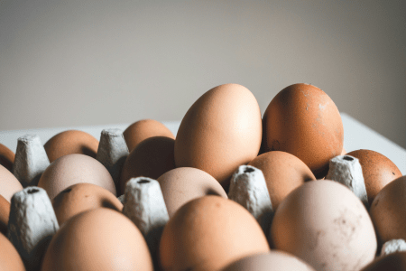 Ovos marrons e brancos dispostos em uma bandeja de papelão, com alguns ovos em destaque em primeiro plano.