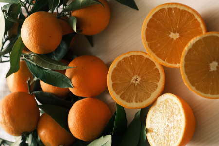 Laranjas inteiras e cortadas ao meio, com folhas verdes, dispostas sobre uma superfície de madeira, destacando a polpa e a casca dos frutos.