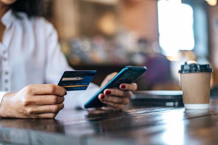 Pessoa usa serviços bancários pelo celular, com o cartão de crédito am uma das mãos.