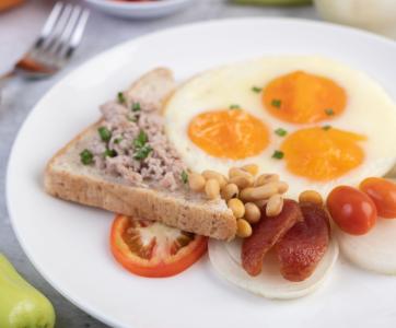 O café da manhã consiste em ovos fritos, linguiça, carne de porco moída, pão, feijão vermelho e soja em um prato branco.