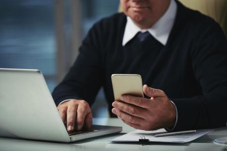 Homem de suéter preto usa autenticação em duas etapas pelo celular e notebook.