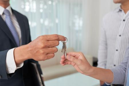 Corretor imobiliário de terno entrega um molho de chaves para um cliente em ambiente interno, simbolizando a conclusão da compra ou locação de um imóvel.
