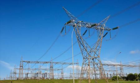 Torres e linhas de transmissão de energia elétrica em uma subestação, sob céu azul, com estruturas metálicas distribuídas por uma área aberta.