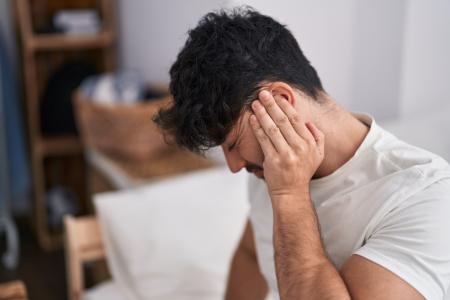 Jovem hispânico com dor nas costas sentado na cama em seu quarto