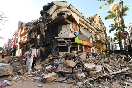 People walk past the rubble of a collapsed building after an earthquake in Pereira, Colombia on August 11, 2026. Colombian volunteers and rescuers cleared rubble with their bare hands to search for survivors early on August 11 after the country's strongest earthquake in a decade killed at least 169 people and smashed dozens of buildings. (Photo by Jaime SALDARRIAGA / AFP) • AFP