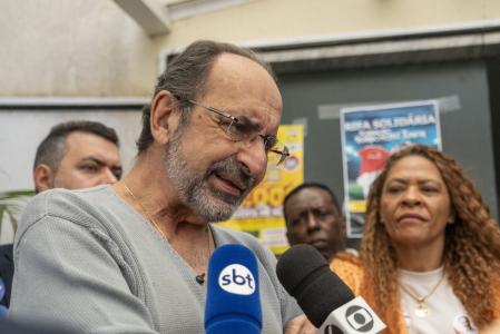 De suéter cinzar e óculos, Alexandre Kalil fala em microfones de duas emissoras com pessoas ao redor