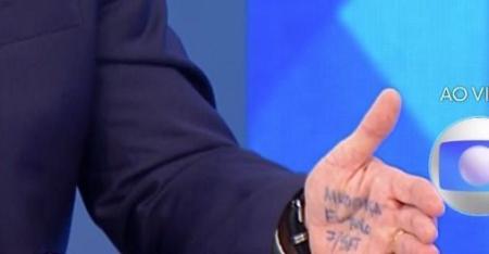 Palma da mão de Flávio Bolsonaro exibindo as palavras 'MUDANÇA', 'FUTURO' e '7/SET' anotadas à caneta durante a transmissão do Jornal Nacional