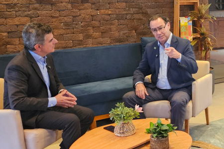 À direita, Augusto Cury, de blazer azul escuro e camisa azul clara, conversa com interlocutor sentado em poltrona cinza