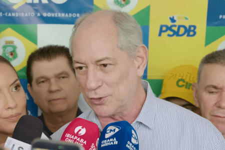 Ciro Gomes fala em entrevista coletiva inclinado na direção de três microfones com banner do PSDB ao fundo