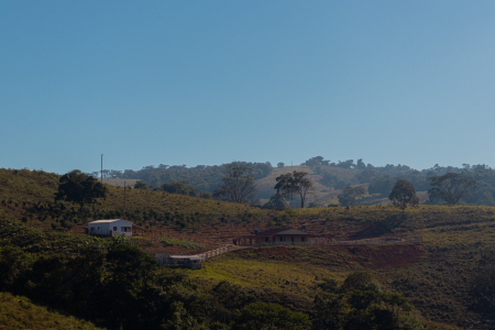 Paisagem de uma propriedade rural, com áreas de pastagem, cercas, árvores e construções ao longo do terreno.