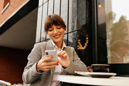 Mulher de camisa branca e paletó sorri enquanto usa o celular para comparar fundos de investimento.