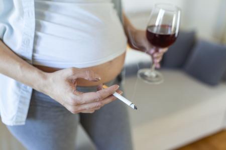 Fumar e consumir álcool durante a gravidez. Mulher com gravidez prolongada que consome álcool e fuma cigarros. Problemas do alcoolismo no período gestacional. Risco de perda do bebê, aborto espontâneo. Alcoolismo