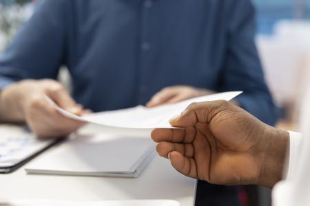 Uma pessoa recebe e analisa um documento financeiro durante uma reunião, representando a formalização de um contrato ou a apresentação de uma proposta relacionada a planejamento financeiro.