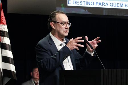 Augusto Cury discursa em púlpito preto à frente da bandeira do estado de São Paulo