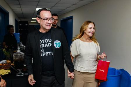 De blusa e blazer pretos, Augusto Cury caminha ao lado de sua esposa, Suleima Cabrera, num corredor de paredes brancas