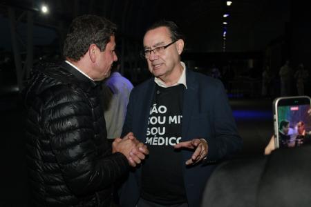 De camisa preta, terno azul e óculos, Augusto Cury conversa com padre que o recebe em evento de música católica