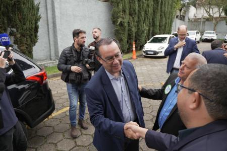 Augusto Cury, cercado de pessoas no que aparenta ser um estacionamento, aperta mão de homem de terno preto
