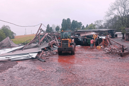 Trator em área rural com estruturas metálicas e construções destruídas ao redor.