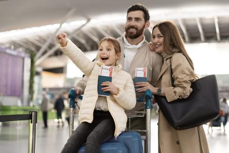 Família com pais e uma criança sorri com os passaportes nas mãos em viagem internacional.