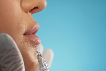 Close-up de uma aplicação de botox cosmético nos lábios femininos. Vista lateral de uma esteticista utilizando uma pequena seringa com um líquido especial para aumentar o volume dos lábios, isolada em fundo azul