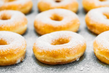 Rosquinhas douradas cobertas com açúcar de confeiteiro, dispostas sobre uma superfície metálica.
